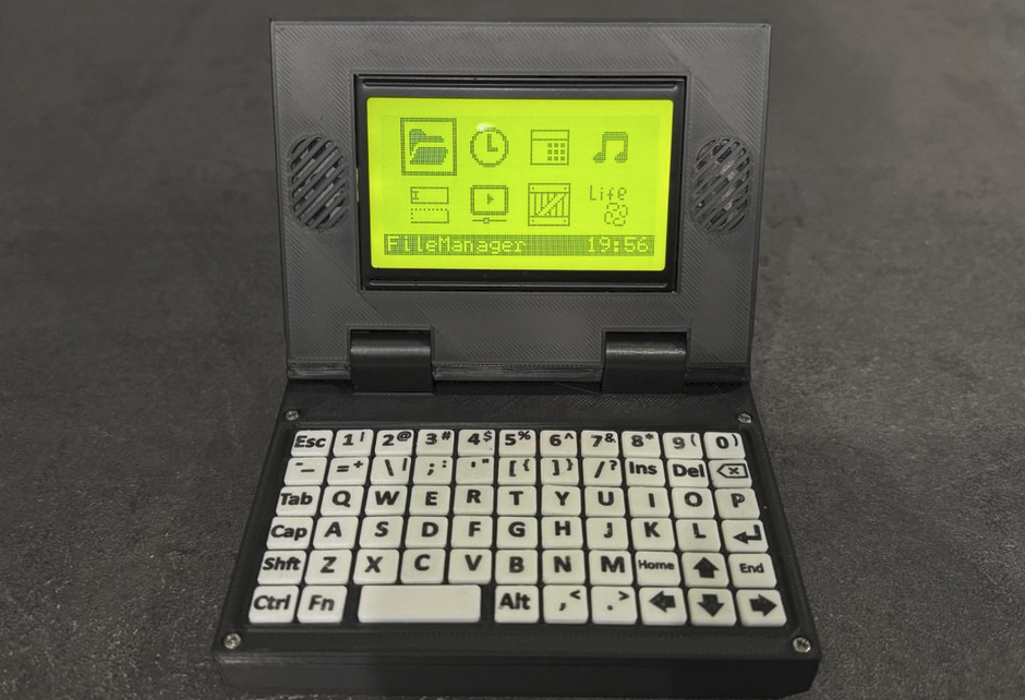 Кастомное DIY-устройство AVR-Laptop на базе микроконтроллера ATmega2560. На маленьком зеленоватом ЖК-дисплее отображается пиксельный графический интерфейс с иконками приложений и открытым файловым менеджером. Портативный гаджет выполнен в раскрывающемся форм-факторе ноутбука серого цвета с миниатюрной механической клавиатурой.