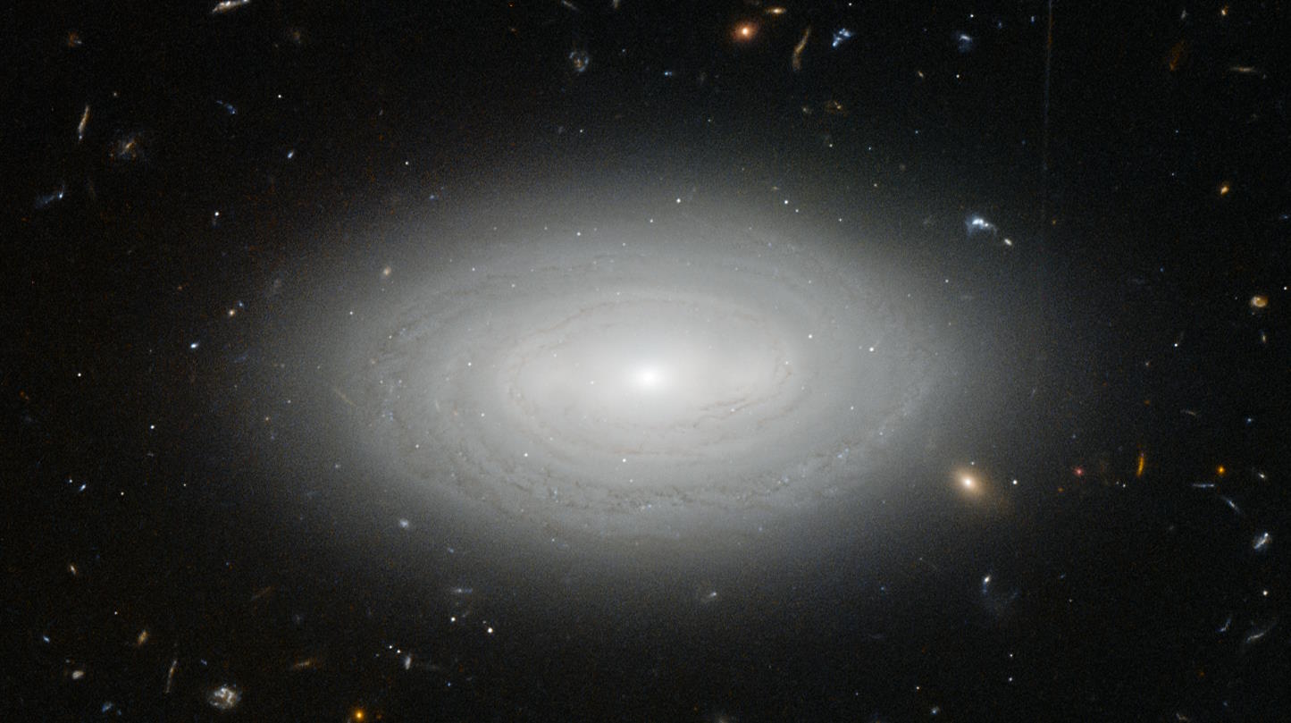  На этом снимке космического телескопа «Хаббл» показана изолированная галактика MCG+01-02-015, расположенная в центре войда, свободного от галактик. В радиусе 100 миллионов световых лет от неё нет других известных галактик, и это, пожалуй, самая одинокая галактика в известной Вселенной. Изолированные дисковые галактики, такие как эта, демонстрируют устойчивое медленное звёздообразование, которое может продолжаться в течение невероятно долгого времени, пока в них сохраняется звёздообразующий газ.