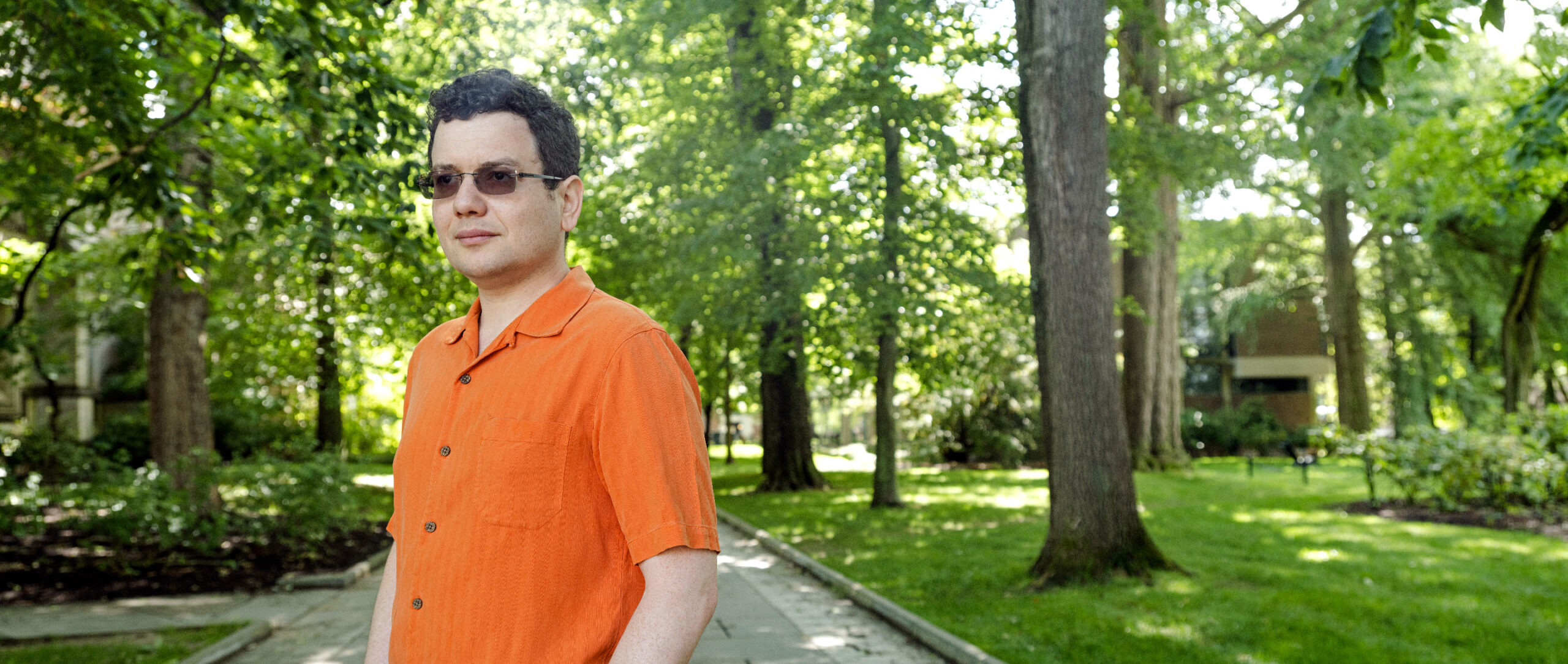 Mark Braverman in an orange shirt in an alley among trees