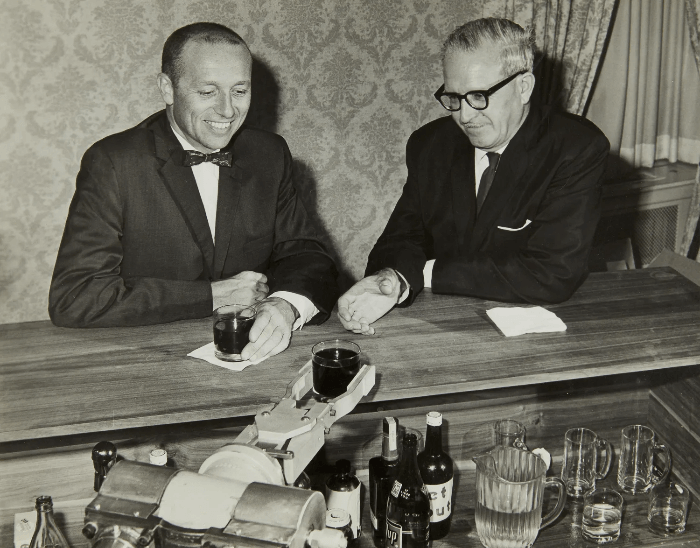 Робот подает напитки сооснователям компании Unimation Деволу (справа) и Энгельбергеру (слева)
