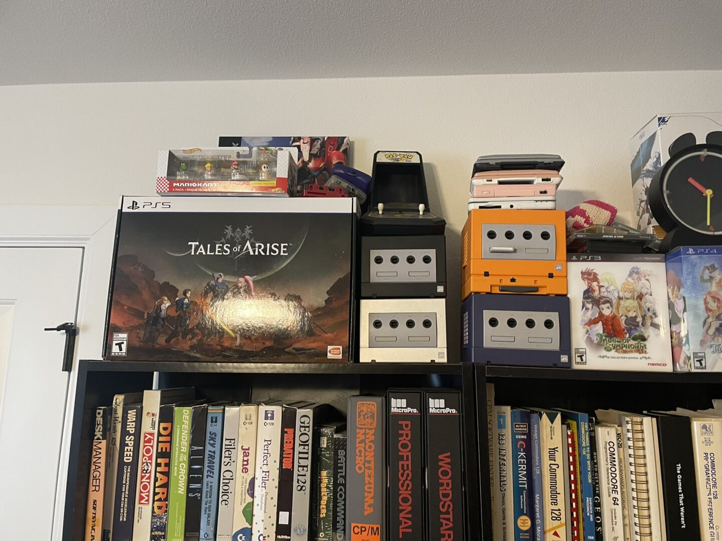Коллекция консолей Nintendo GameCube и Nintendo DS стоит на книжной полке, заставленной компьютерной классикой.  