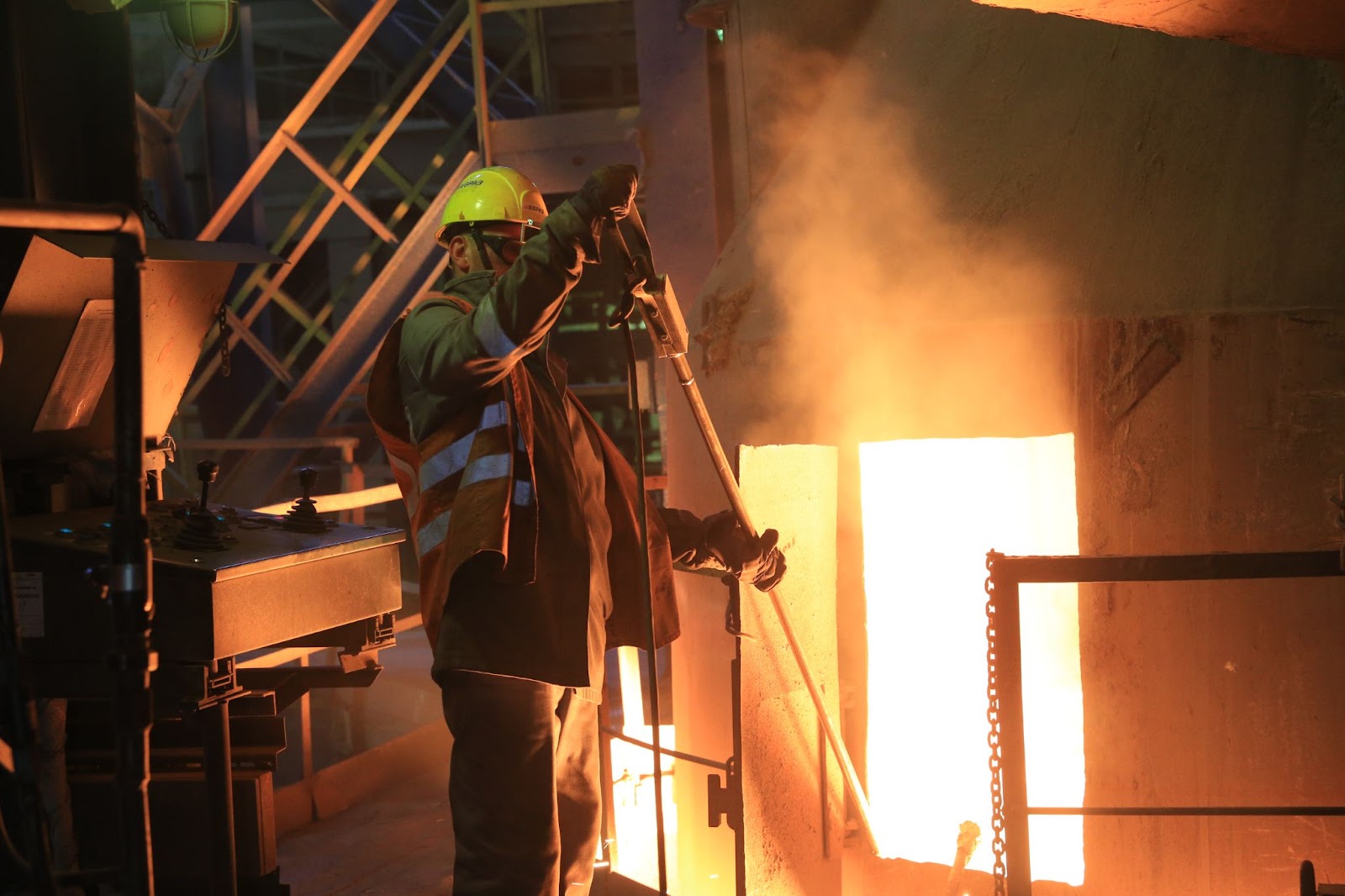 Бетономешалка мешает  бетон, а сталевар берет пробу на химический состав и замеряет температуру металла