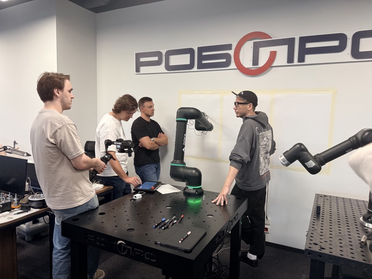 Испытательная ячейка во время отладки. Робот закреплён на рабочей платформе, на стене тестовые полотна, а команда разбирает результат