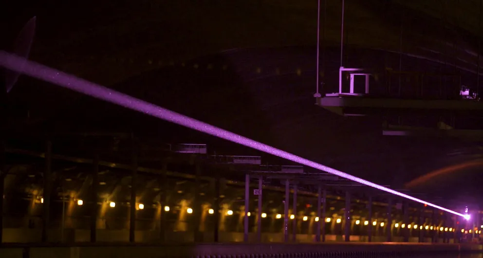 Узкий фиолетовый луч освещает тёмную комнату. В 2019 году при проведении эксперимента таким лазерным пучком было успешно передано 400 Вт на расстояние 325 м