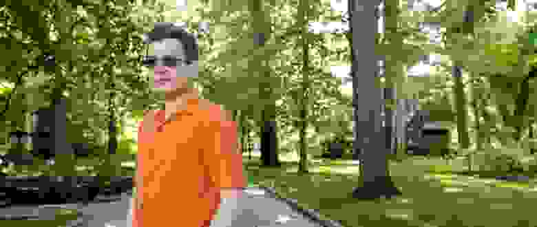 Марк Брейверман в оранжевой рубашке на аллее среди деревьев
