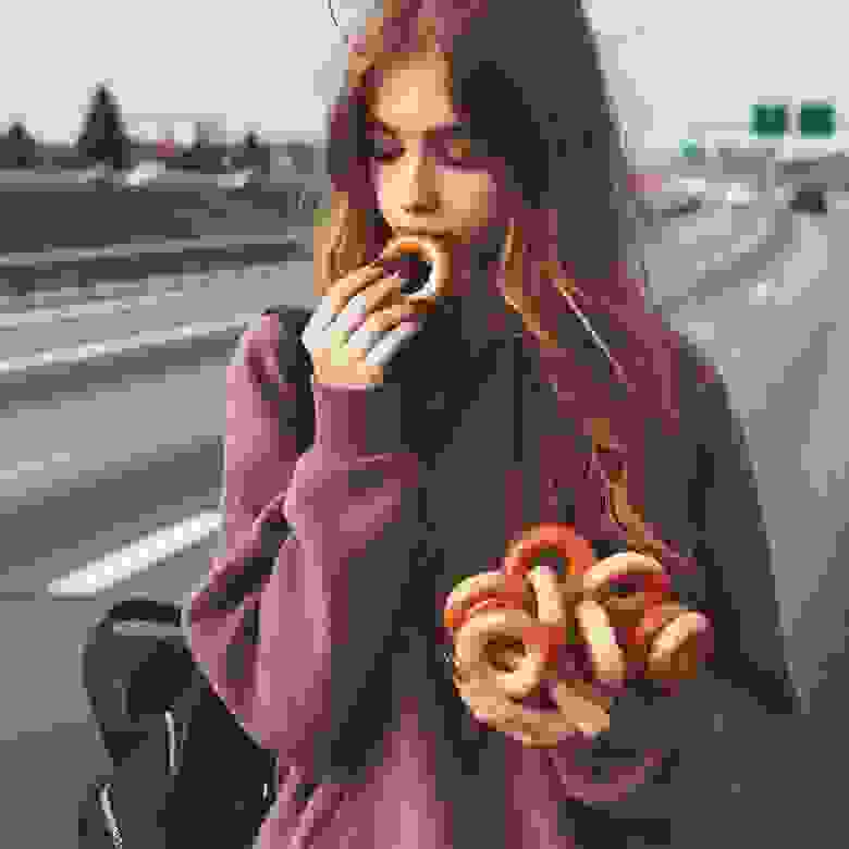 Teenage girl is walking down by highway. In  her right hand she is holding two traditional Eastern European small,  crunchy, mildly sweet bread rings, very small in size.