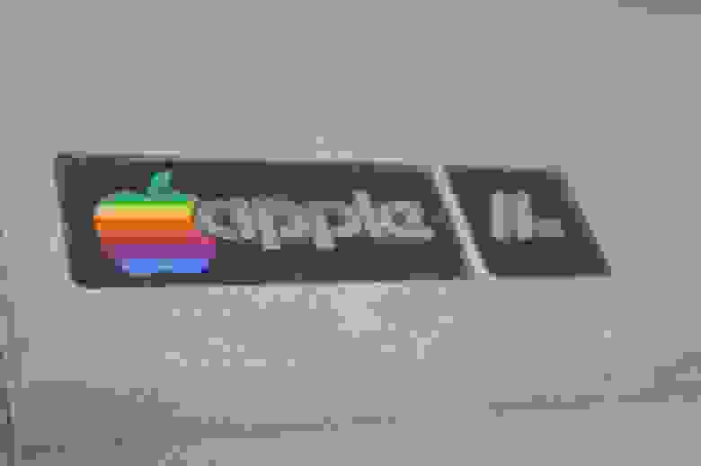 Фирменный значок Macintosh - цветное еще тогда яблочко. Модификация - Apple IIe. Отличается от оригинальной "двойки" кроме внешнего вида увеличенной оперативкой (Было 4/48КБ на выбор, стало 64 КБ), более дешевыми чипами ну и прочими не очень большими изменениями, для которых маркетологи решили не выпускать  новый Мак, а просто добавить буковку к названию)

